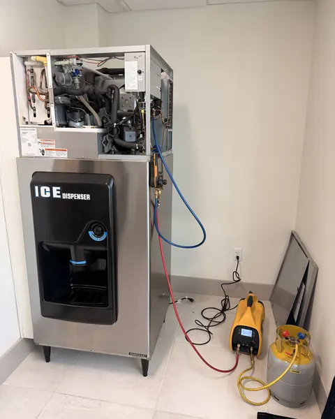 Hoshizaki commercial ice machine with ice dispenser opened up for repair, with refrigerant gauges and a recovery machine connected